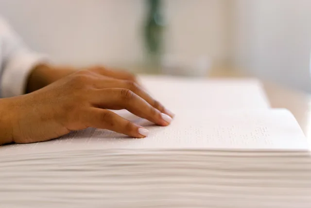 Close-up of a person's hand reading a Braille book, highlighting accessibility and tactile reading. Accessibilità dei contenuti social