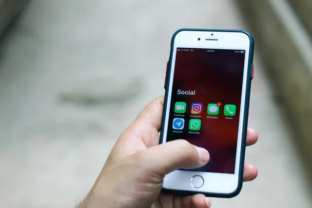 Hand holding a smartphone displaying various social media and communication apps. Formati social per i brand