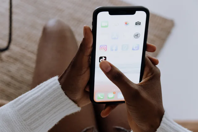 Close-up of hands with a smartphone using the TikTok app indoors, reflecting modern mobile technology. Limitare i permessi delle applicazioni collegate
