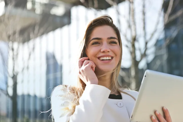 Confident businesswoman using her tablet and phone, smiling outdoors in sunlight. Profili aziendali e credibilità