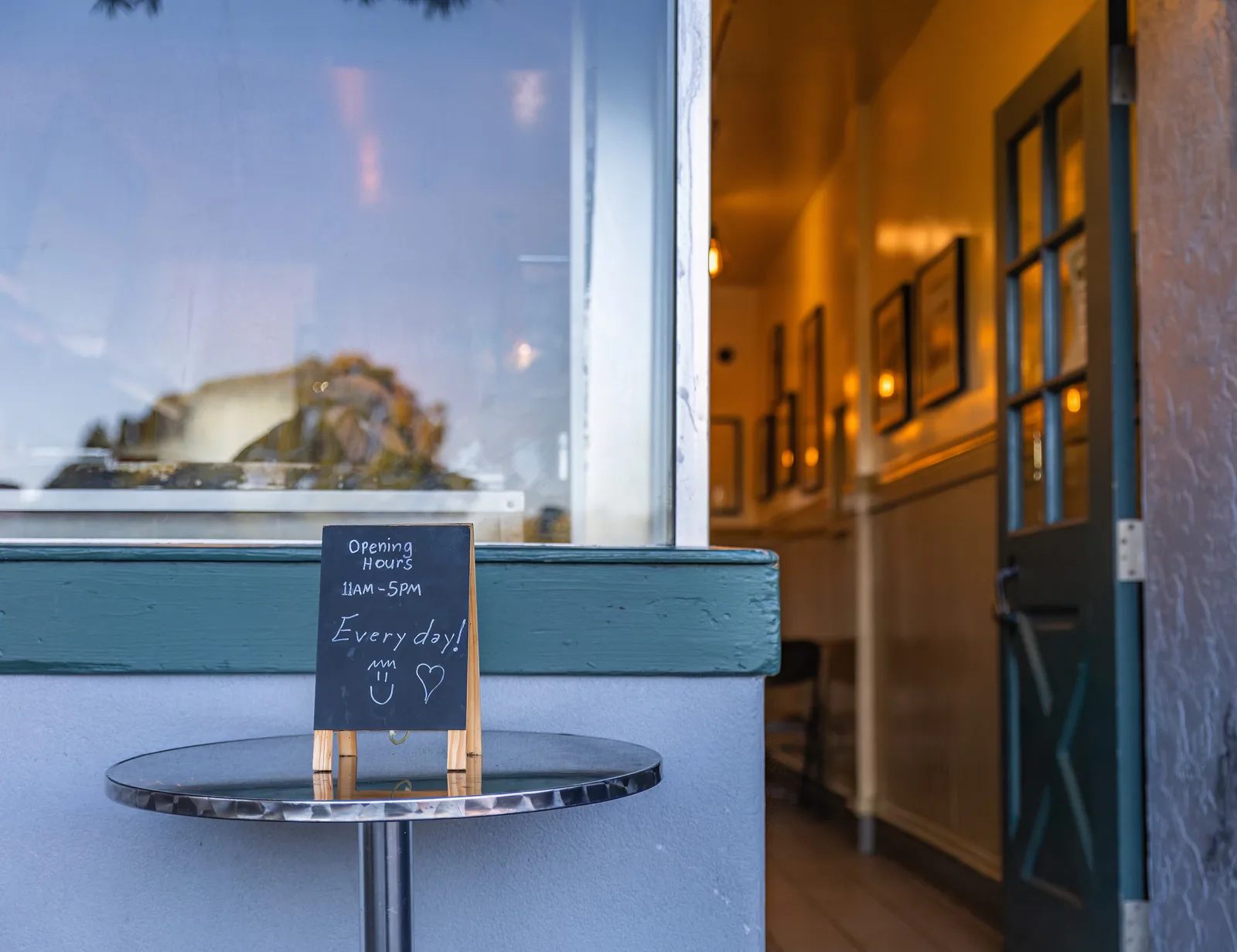Entrance of a charming café with a chalkboard displaying opening hours from 11am to 5pm