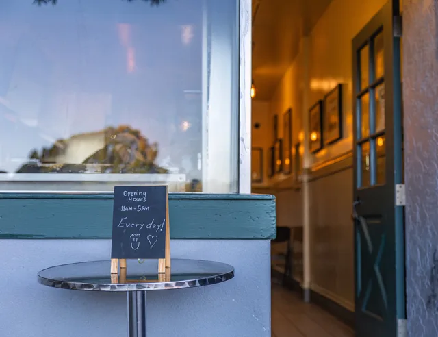 Entrance of a charming café with a chalkboard displaying opening hours from 11am to 5pm. Social per attività locali